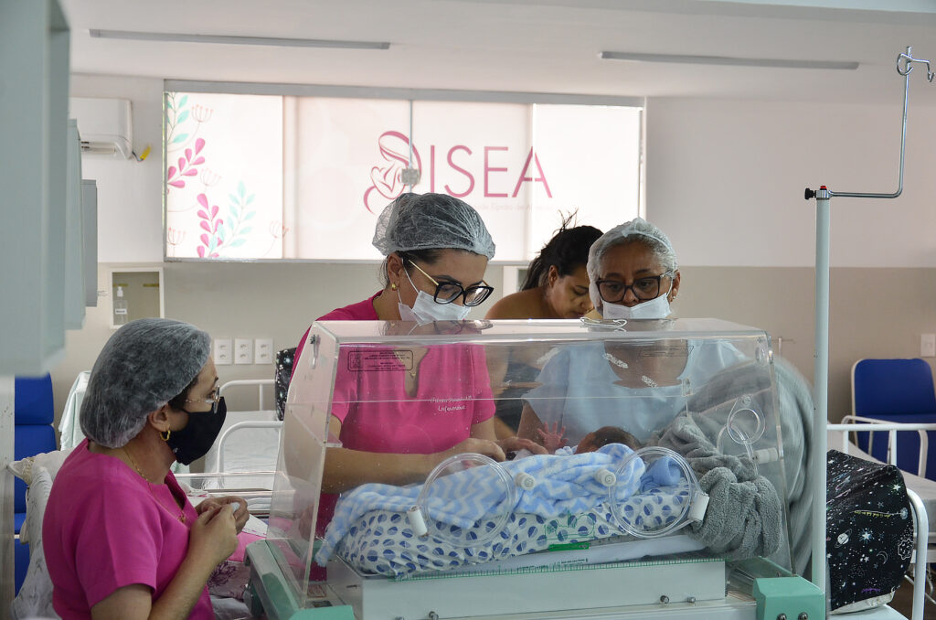 Imagem de enfermeiras cuidando de recém-nascido em incubadora.