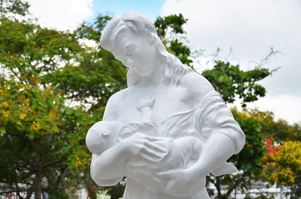 Estátua branca de mulher segurando filho no colo.