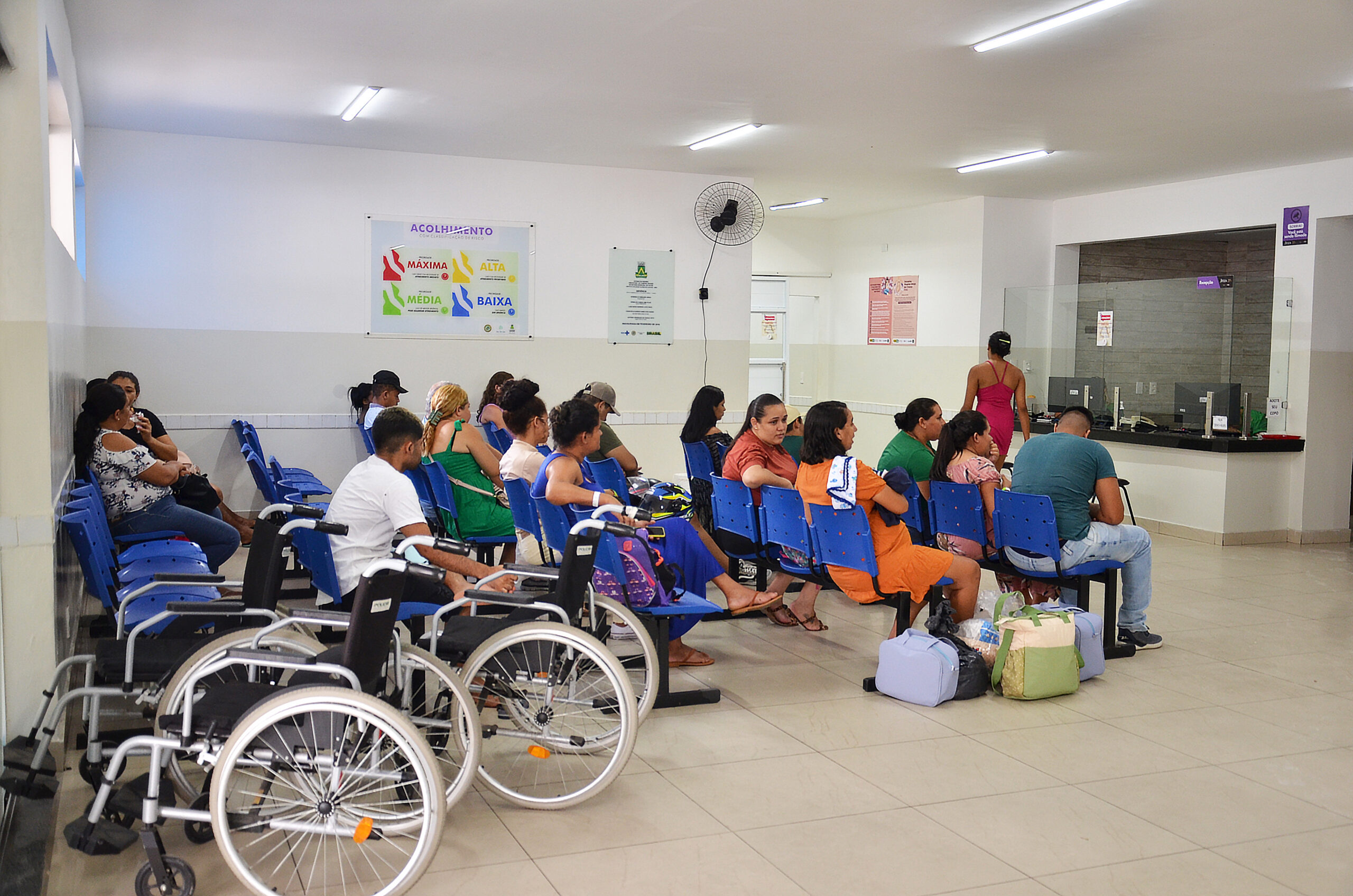 Recepção de maternidade com gestantes sentadas e cadeiras de roda.